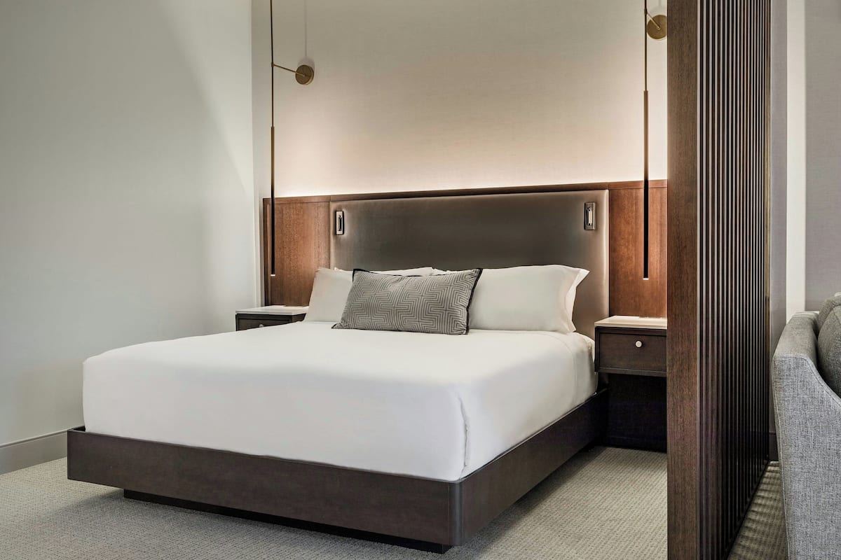 A modern hotel room with a large bed, wooden headboard, and two bedside tables.