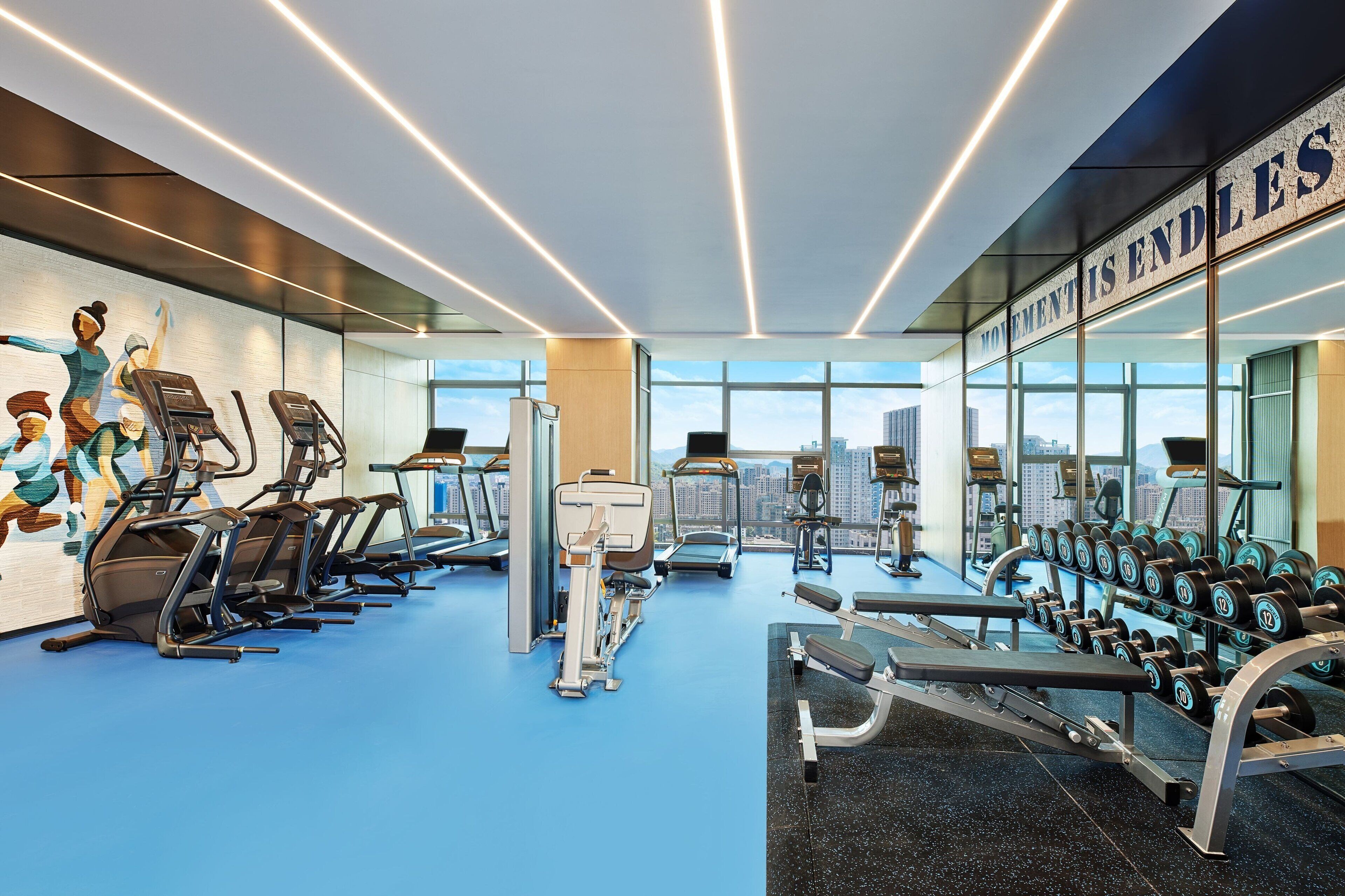 A modern gym with exercise equipment, large windows, and motivational wall art.