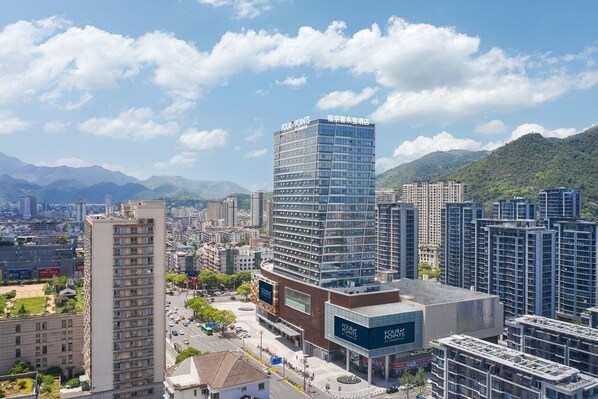 Un hotel moderno de gran altura, con fachada de vidrio, rodeado de otros edificios y montañas al fondo.