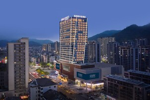 Un hotel de gran altura con varios pisos, un cartel llamativo y vistas de la ciudad y montañas circundantes.