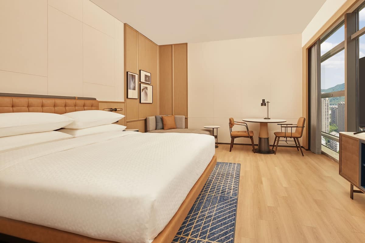Una habitación de hotel con una cama grande, una pequeña mesa de comedor y vistas a la ciudad.