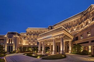 A grand hotel entrance with a classical facade, large columns, and a well-lit driveway.