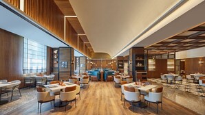 Un amplio vestíbulo de hotel con varias zonas de estar, un bar central y paneles de madera en las paredes.