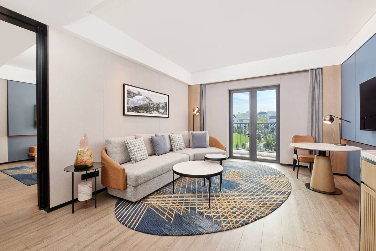 Ein modernes Wohnzimmer mit einer Couch, einem Couchtisch und einem Esstisch, einem großen Fenster mit Blick auf die Stadt und einem Flachbildfernseher.