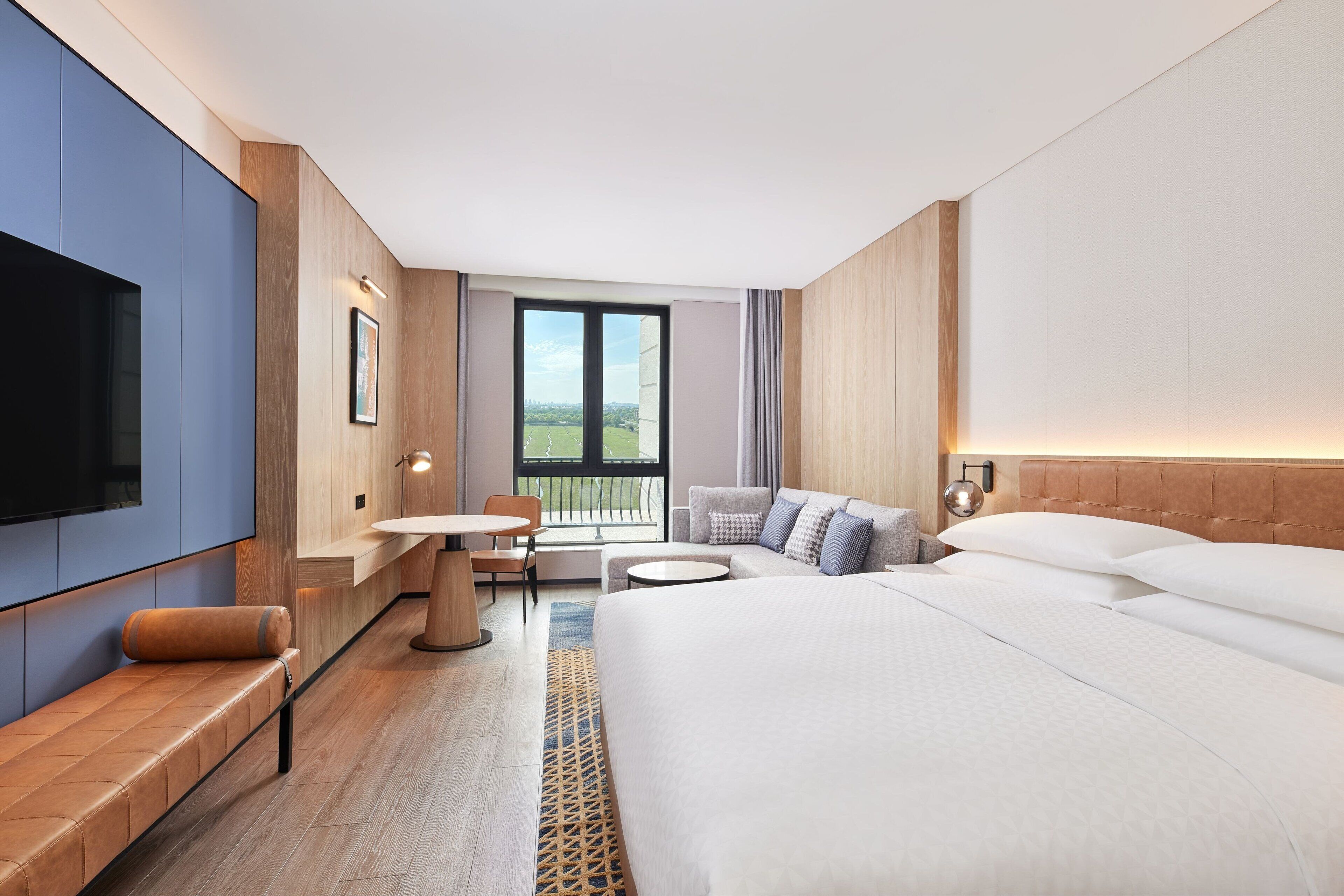 Una habitación de hotel moderna con una cama grande, un área de descanso con una mesa, un televisor y un balcón con vistas.