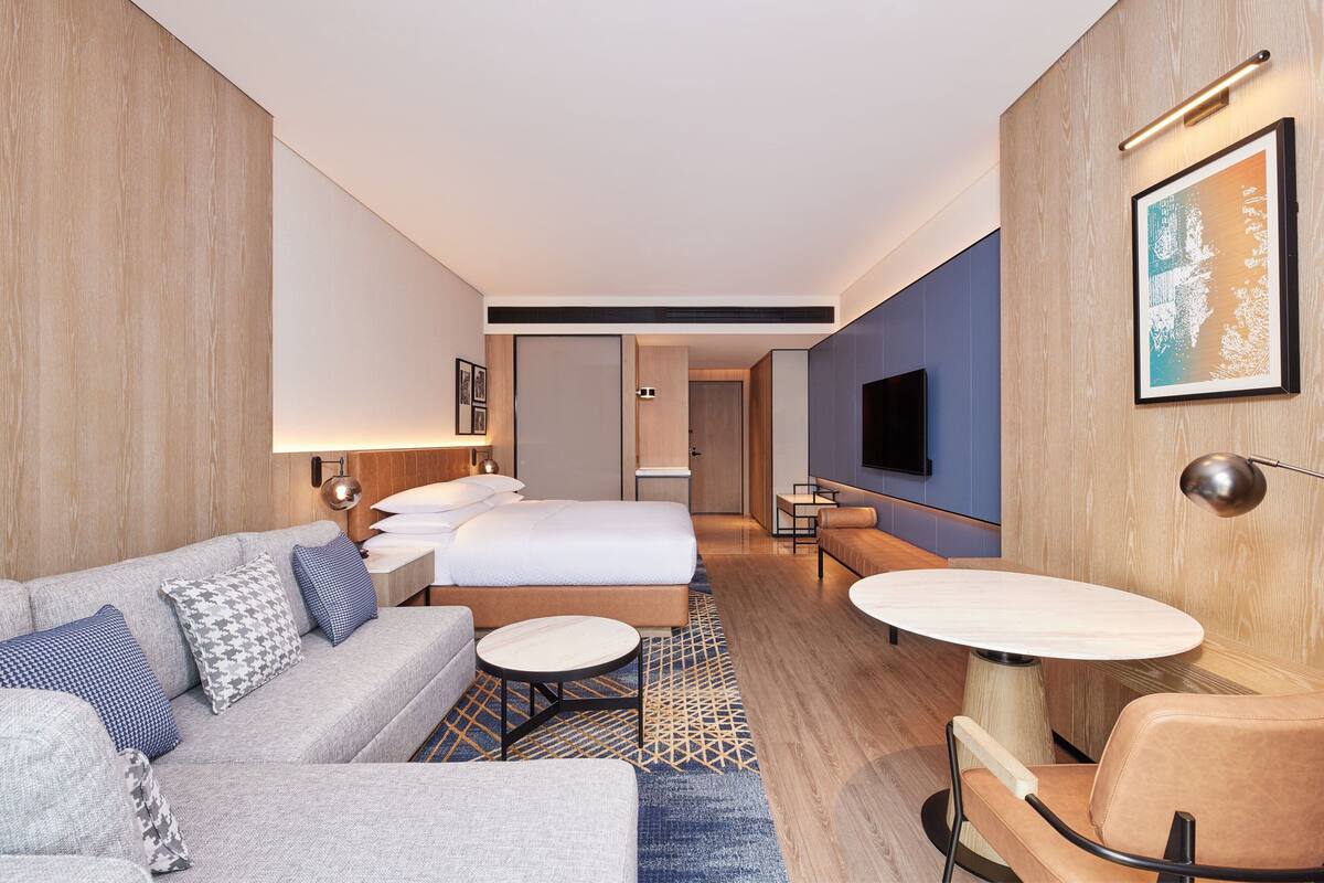 Ein modernes Hotelzimmer mit einer Couch, einem Bett, einem runden Tisch und einem Fernseher.