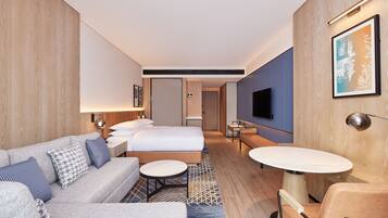 Una habitación de hotel moderna con sofá, cama, una mesa redonda y televisor.