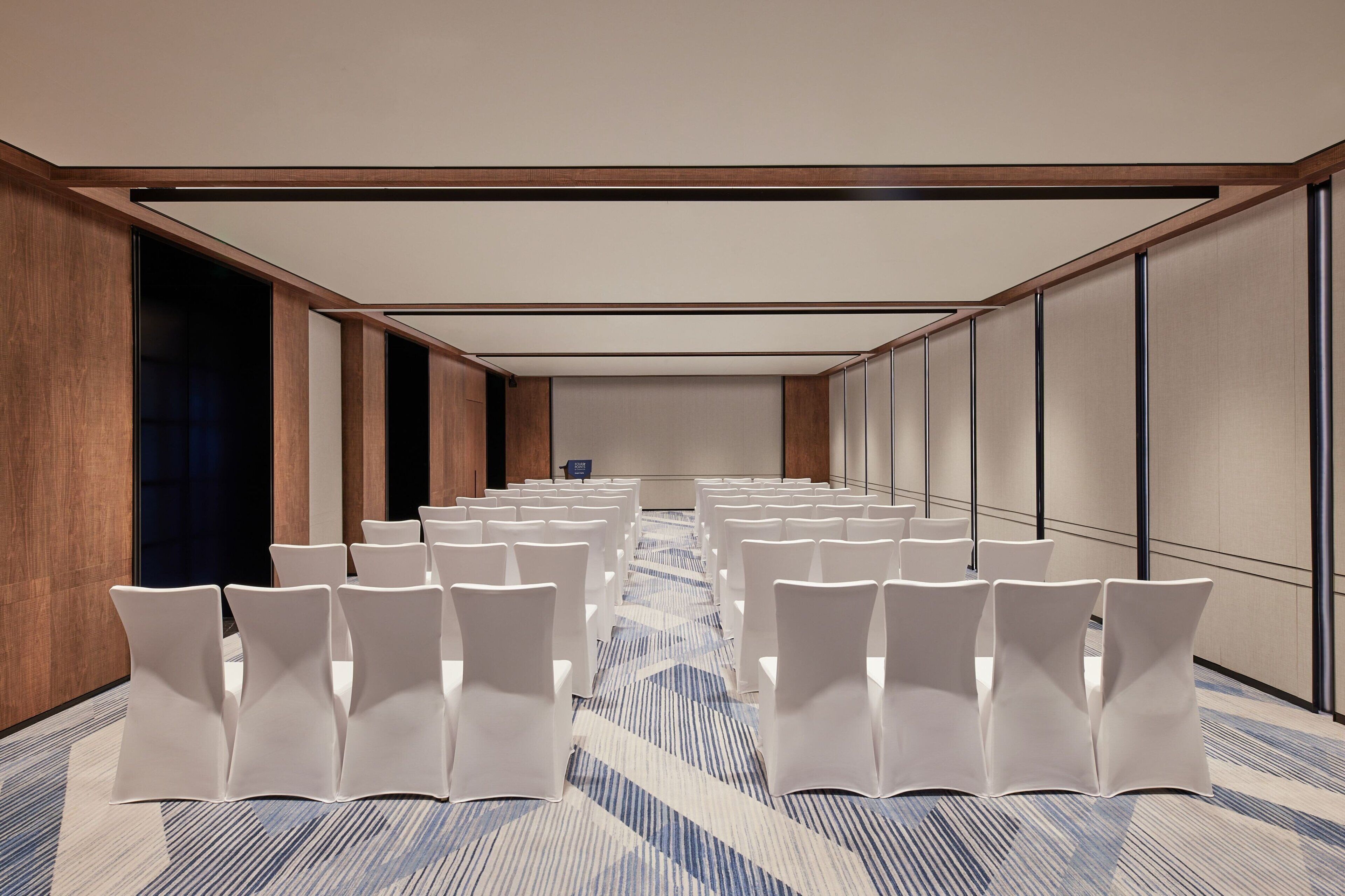 Un salón de conferencias con filas de sillas blancas, suelo alfombrado y techo de madera.