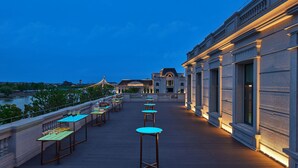 Terraza en la azotea con mesas y sillas, con vistas a un cuerpo de agua y edificios.