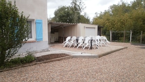 Un patio de grava con una mesa y sillas, un espacio exterior cubierto y un edificio con un persiano azul.