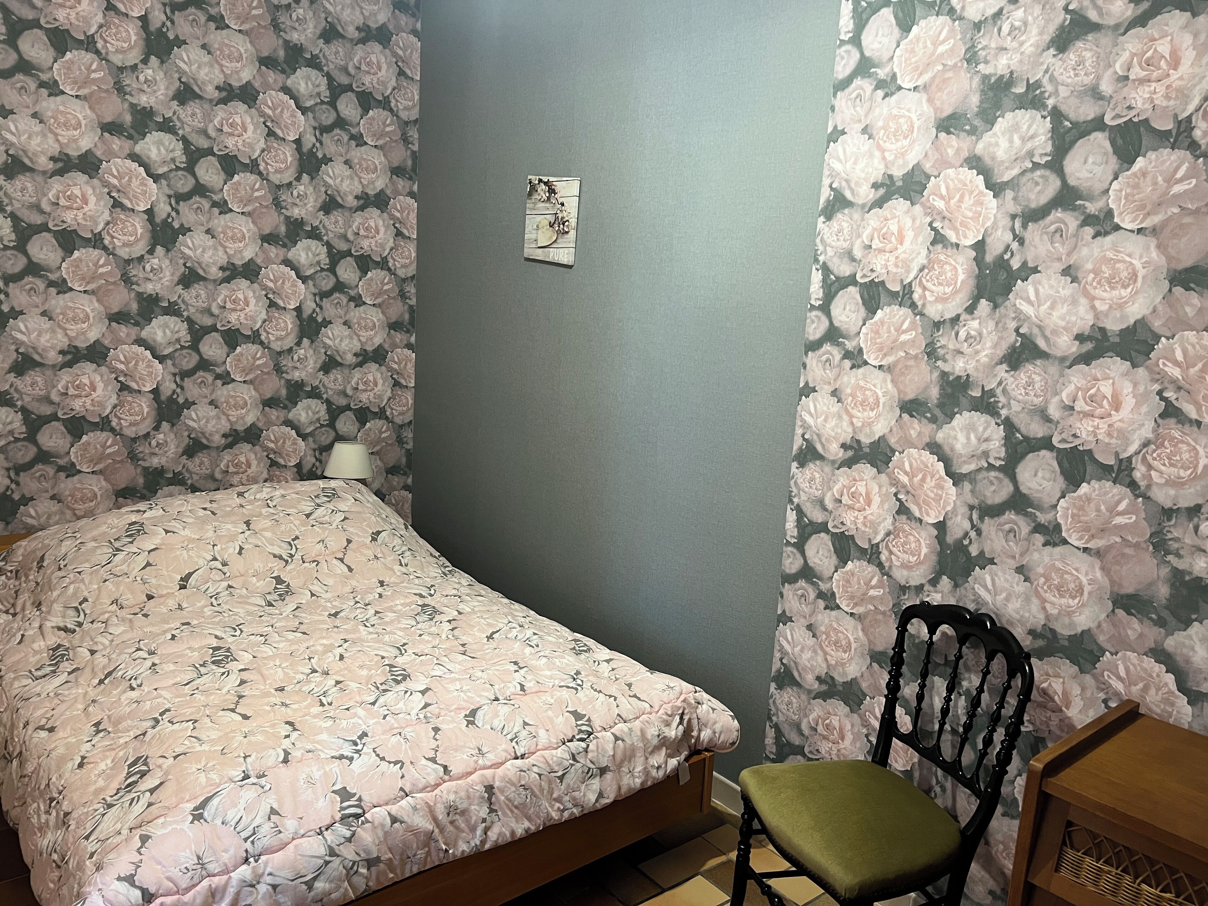 A bedroom with a bed, a chair, and floral wallpaper.