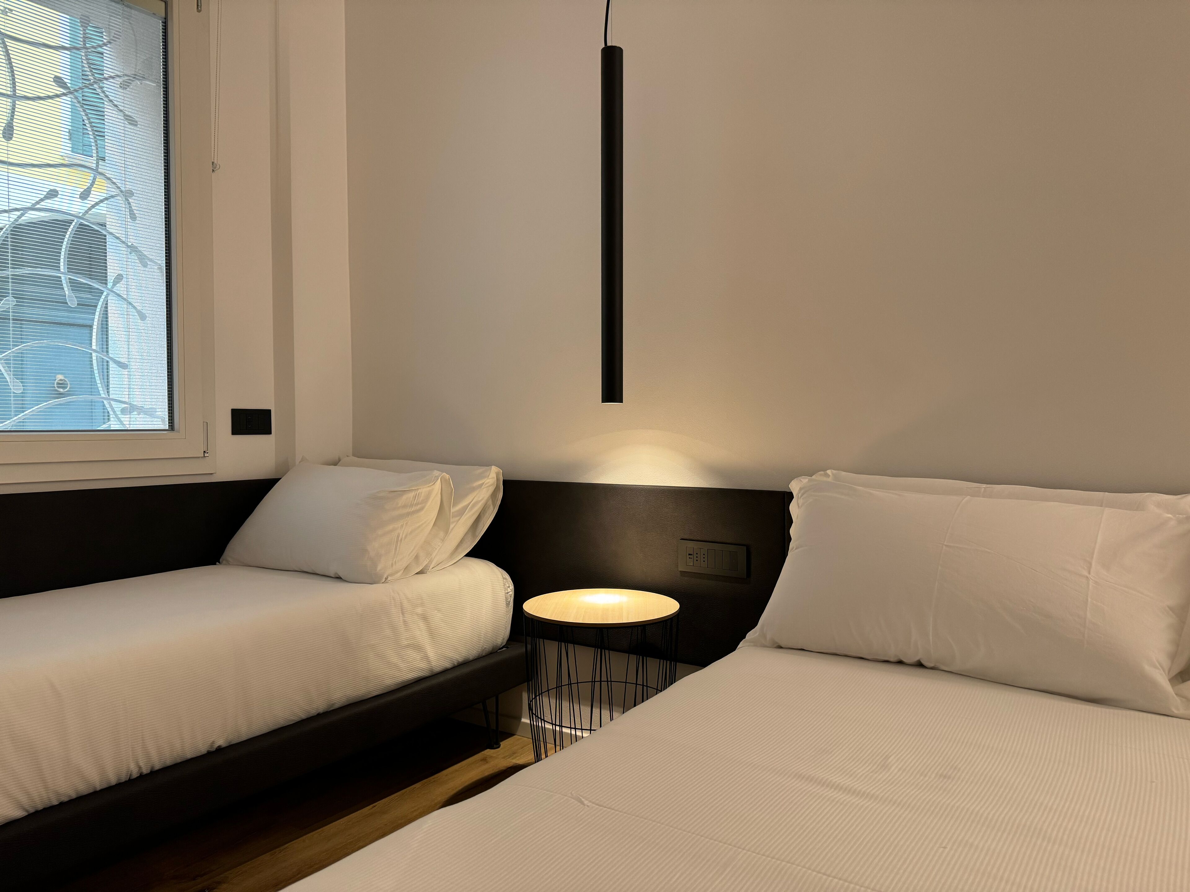 A modern hotel room with a bed, a small table, and a window with blinds.