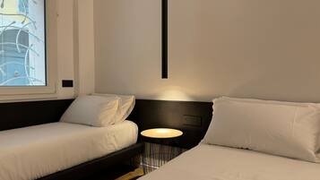 A modern hotel room with a bed, a small table, and a window with blinds.
