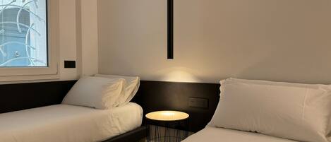 A modern hotel room with a bed, a small table, and a window with blinds.
