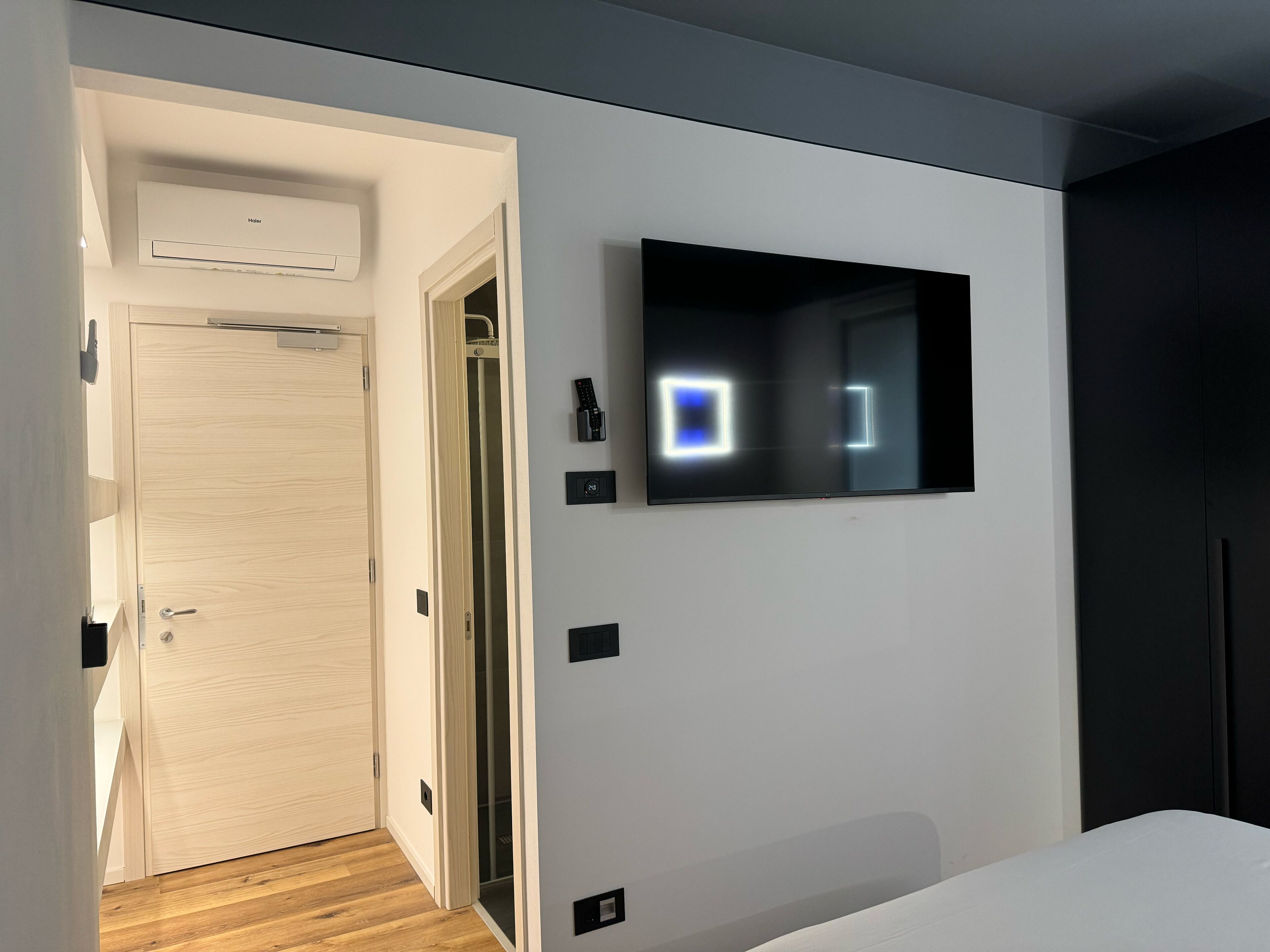 Ein modernes Hotelzimmer mit Holztür, einem angebrachten Fernseher und einem Kleiderschrank.