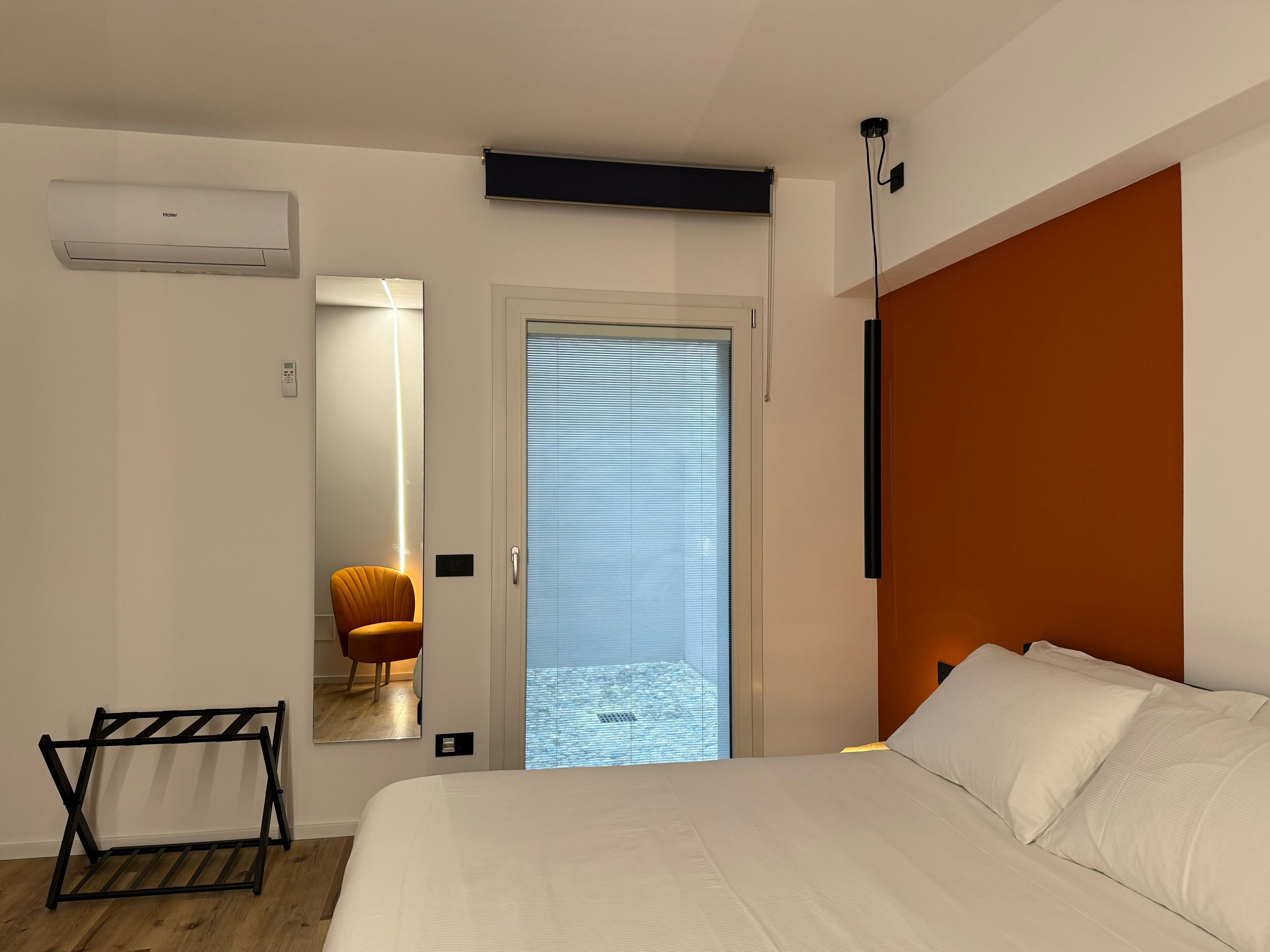 A modern bedroom with a bed, a chair, a black metal rack, and a door leading to a balcony.