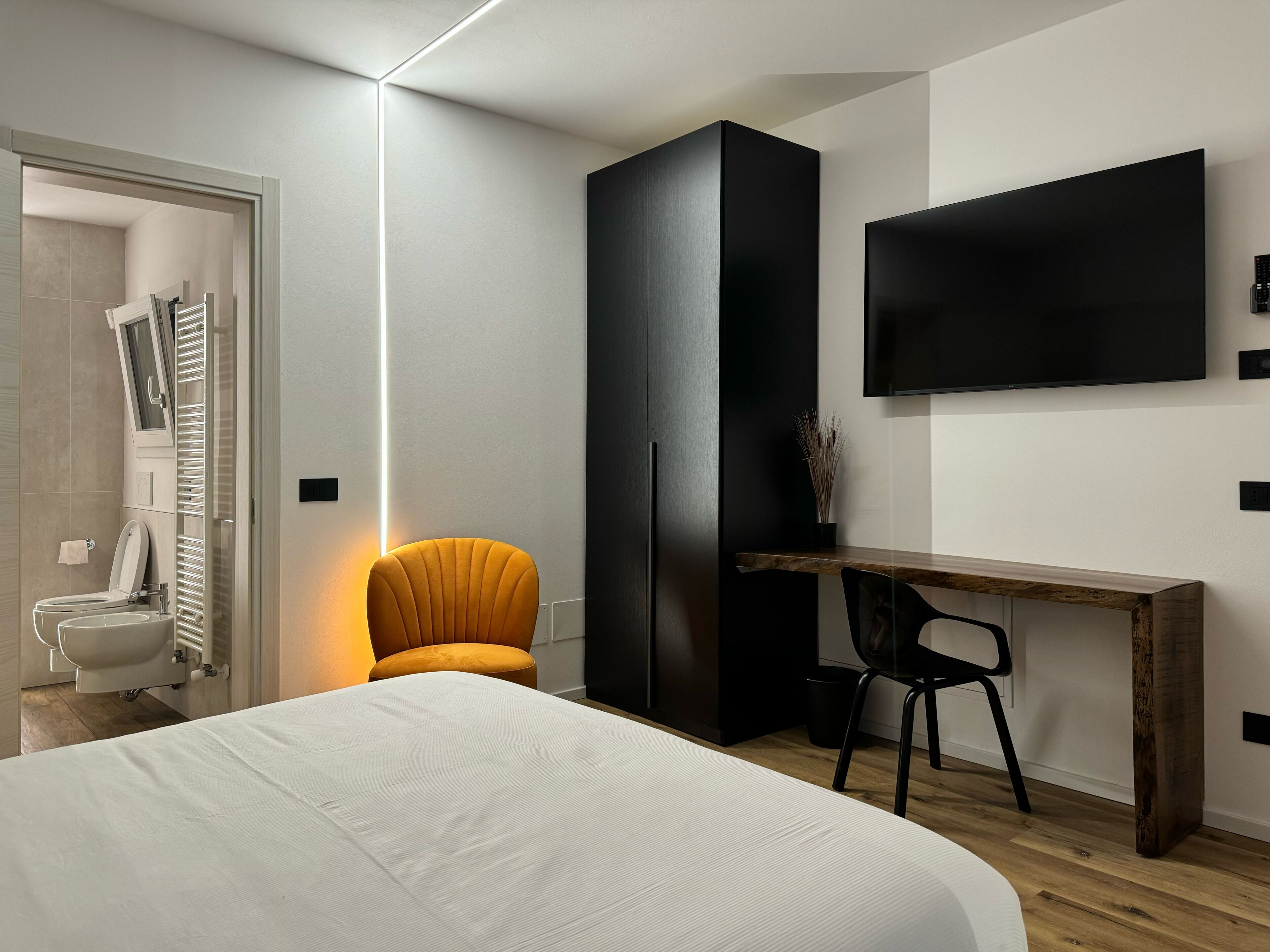 Quarto de hotel moderno com uma cama, escrivaninha, cadeira, televisão e guarda-roupa.