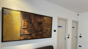 Eine moderne Hotelhalle mit einem großen, abstrakten Gemälde, einem braunen Sofa und zwei Türen mit den Aufschriften 03 und 04.