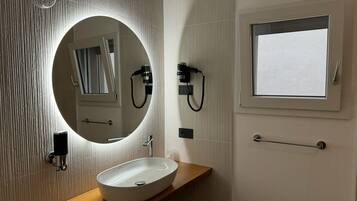 A bathroom with a round mirror, a white sink, a towel rack, and a window.