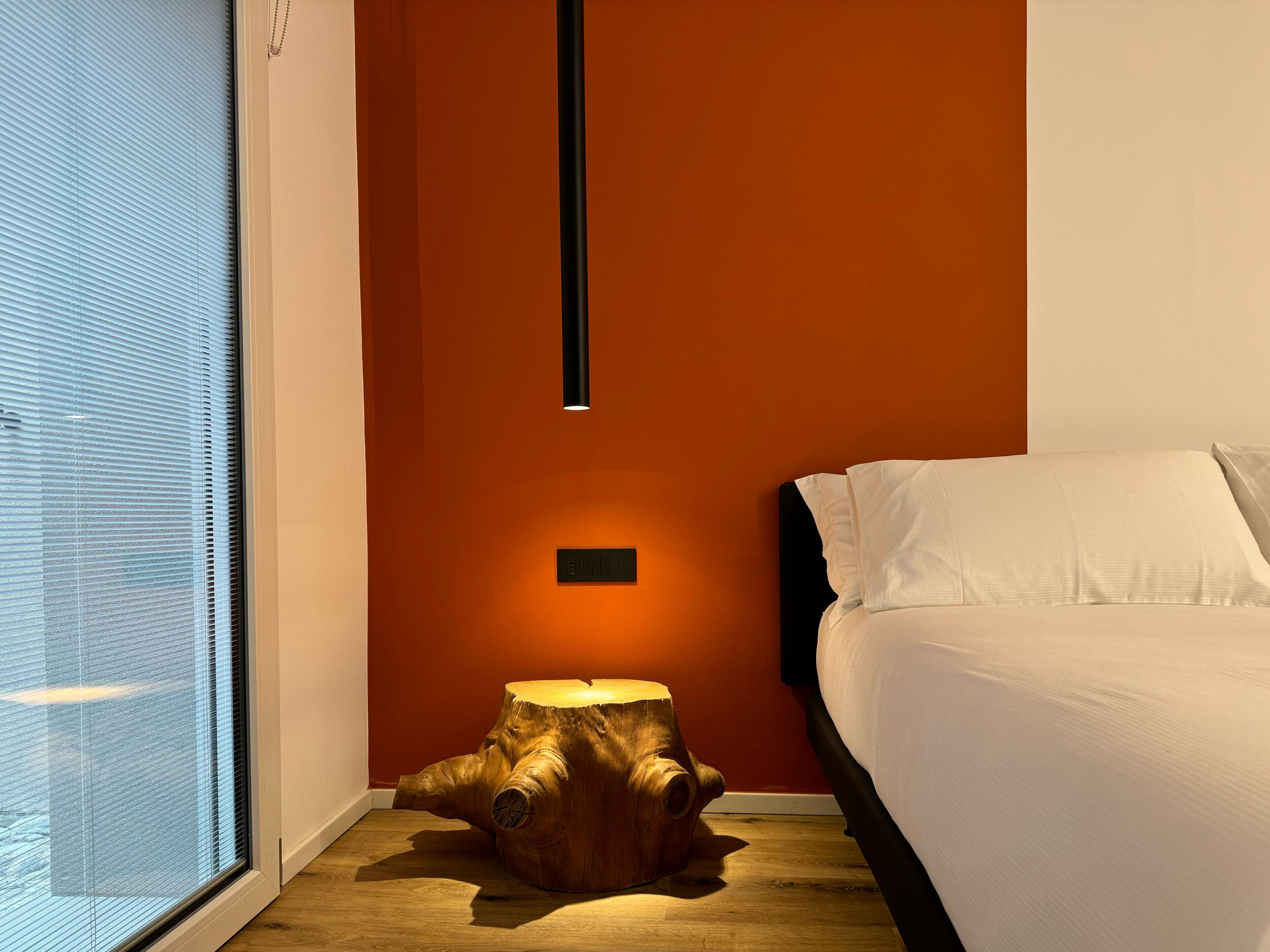 Un dormitorio con una cama, una mesita de noche, una lámpara de pared y una ventana con persianas.