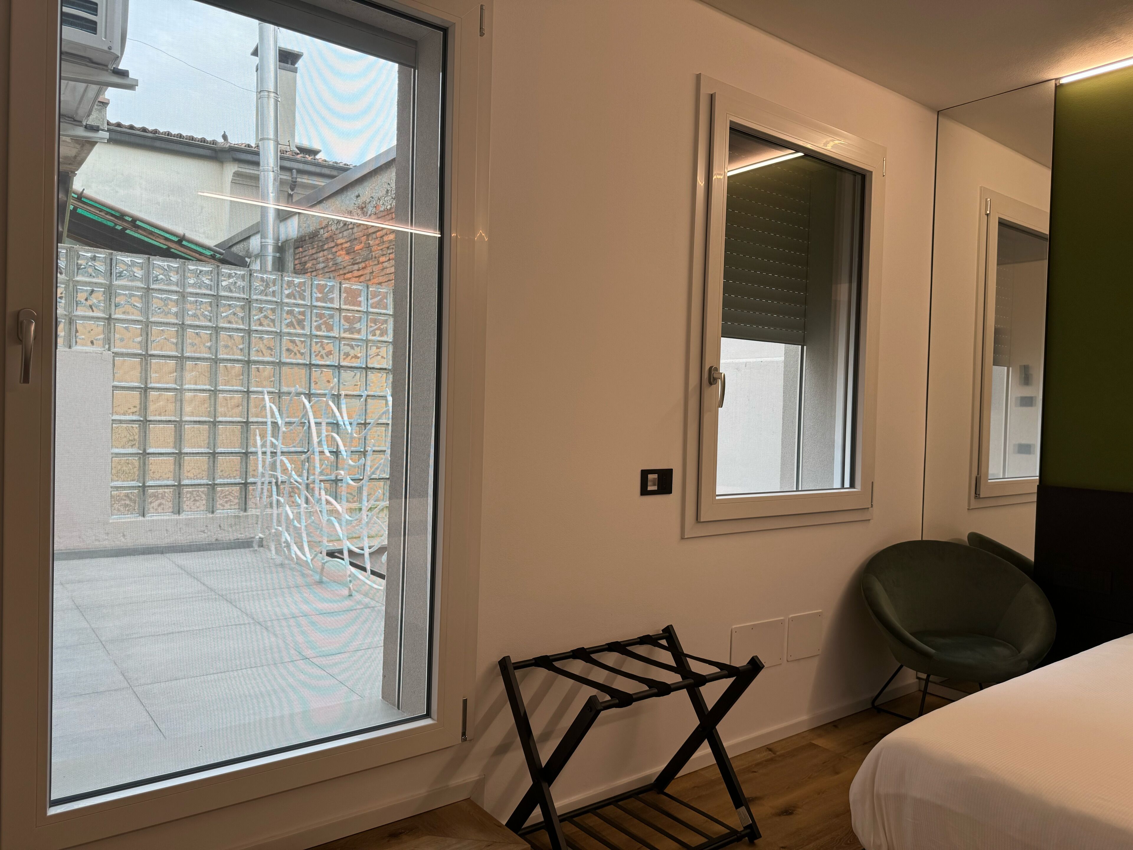 A room with a sliding glass door to a courtyard, a bed, a chair, and a wall-mounted drying rack.