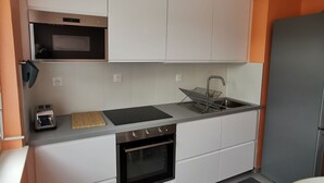 Cocina compacta con armarios blancos, microondas, tostadora, lavaplatos y refrigerador.