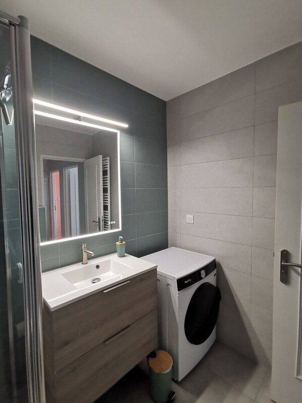 A modern bathroom with a white sink, mirror, and a front-loading washing machine. - Appartement Spacieux ,calme et Proche du Centre. Idéal Pour Visiter L'alsace (Mulhouse)