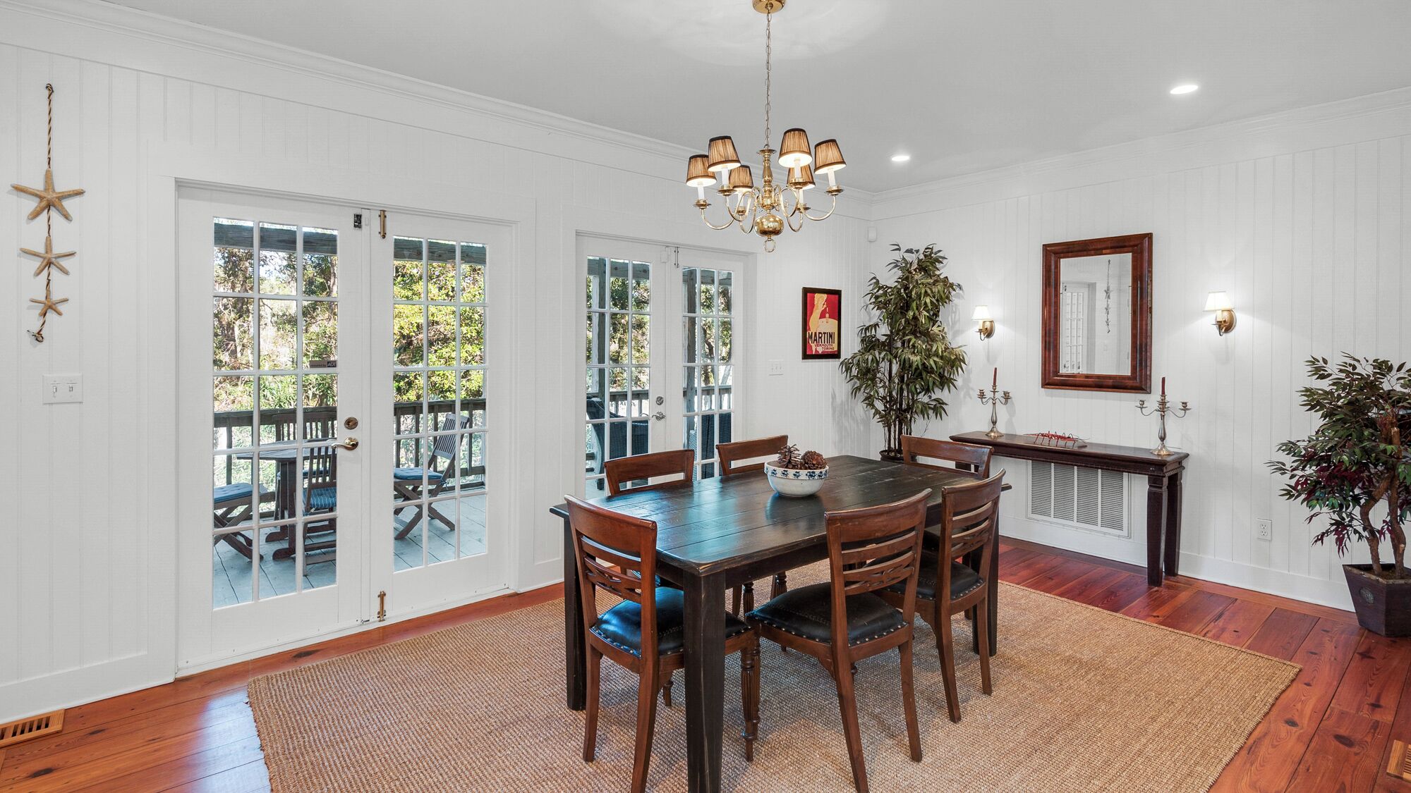 A dining room with a wooden table and chairs, a chandelier, and a large window with a view of the outdoors.