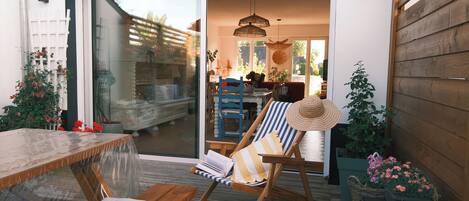 A wooden deck with a table and chairs, a sliding glass door leading to an interior space, and potted plants.