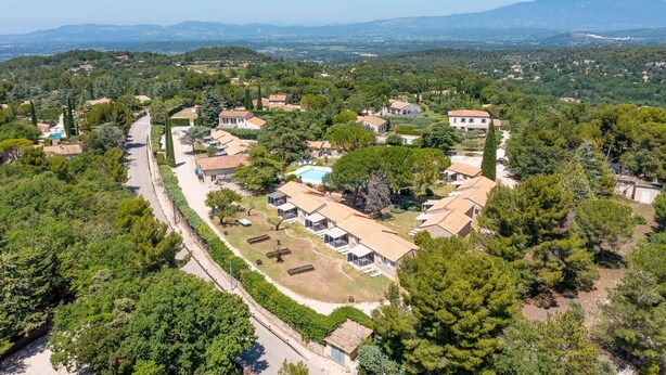An aerial view of a residential area with houses, a road, and surrounding greenery. - Rental in a quiet setting with pool n°5 (La Roque-sur-Pernes)