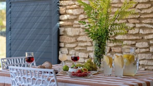 A table with a striped tablecloth, a glass pitcher, a glass of red wine, a glass of white wine, a glass of lemonade, a bowl of fruit, and a potted plant. - Rental in a quiet setting with pool n°5 (La Roque-sur-Pernes)