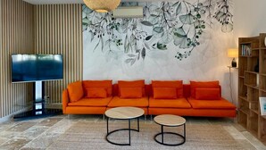 A living room with a sofa, two coffee tables, a TV, a wall-mounted air conditioner, and a bookshelf. - Cottage with AC and terrace n°10 (La Roque-sur-Pernes)
