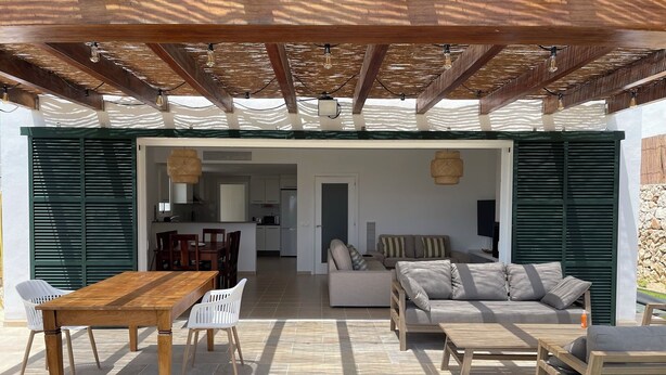 An open-plan living area with a wooden table and chairs, a sofa, and a cushioned bench. - Villa Can Simo Menorca (Sant Lluis)