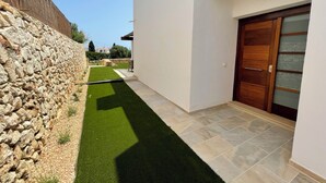 A modern house with a stone wall, a paved patio, and a wooden door. - Villa Can Simo Menorca (Sant Lluis)