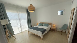A bedroom with a bed, bedside lamps, a chair, a window with curtains, and a ceiling light fixture. - Villa Can Simo Menorca (Sant Lluis)