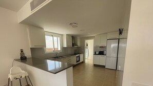 A modern kitchen with a central island, a built-in oven, a microwave, and a refrigerator. - Villa Can Simo Menorca (Sant Lluis)