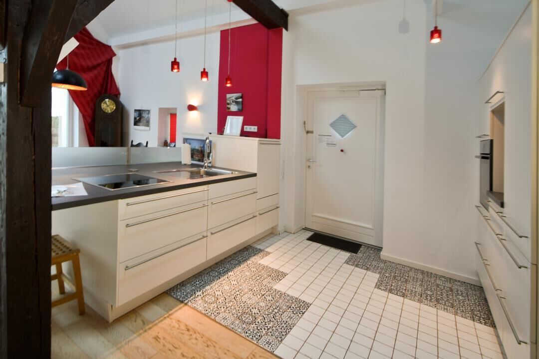 A modern kitchen with a central island, white cabinetry, and a red accent wall.