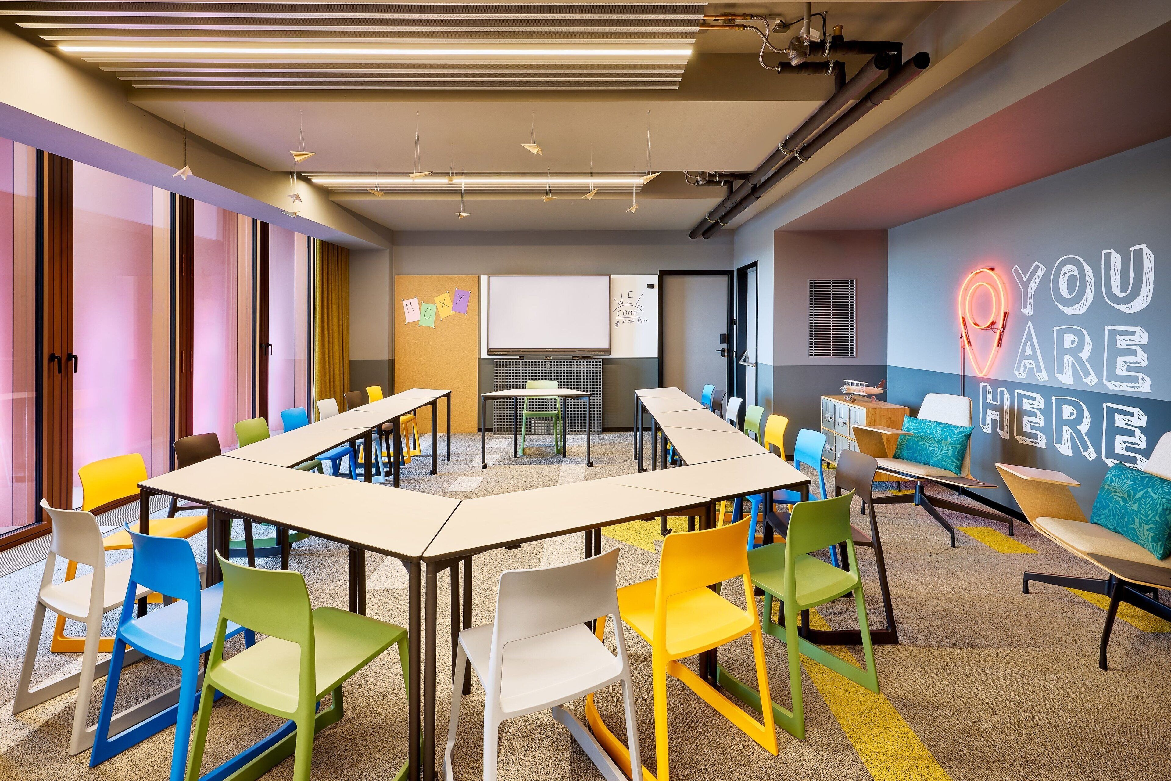 A modern meeting room with colorful chairs, a long table, and a motivational wall sign.