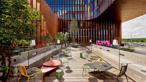 Een terras met diverse stoelen en tafels, omringd door een modern gebouw met grote ramen.