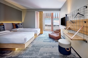 A modern hotel room with two beds, a large window, a TV mounted on a wall, and a wooden bench. - Moxy Luxembourg Airport (Sandweiler)