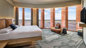 Een moderne hotelkamer met een groot bed, een zithoek en uitzicht op het vliegveld.