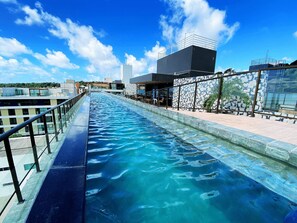 Una piscina con barrera de cristal, rodeada de edificios modernos y un cielo despejado.