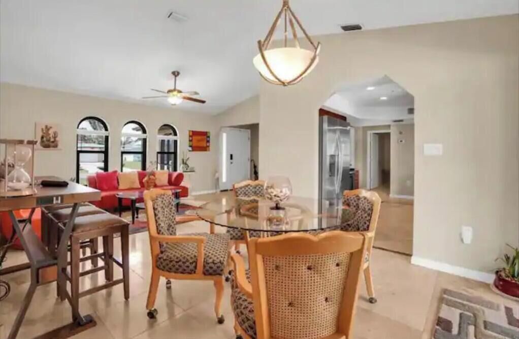 A spacious living room with a glass dining table surrounded by chairs, a red sofa, and a ceiling fan.