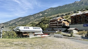 Un chalet de montagne avec un grand bâtiment blanc, des cabanes en bois et une vue sur les collines environnantes.