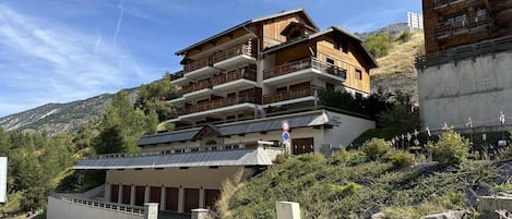 A multi-story hotel with balconies, a covered entrance, and a mountainous backdrop.