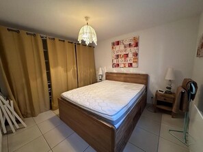 Un dormitori amb un llit de fusta, un penjall, una paret amb la inscripció 'Home Sweet Home' i una petita taula de nit amb una làmpada.