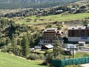 Un edifici d'altes plantes amb terrat pla, envoltat de vegetació i altres edificis en una zona amb pendent.