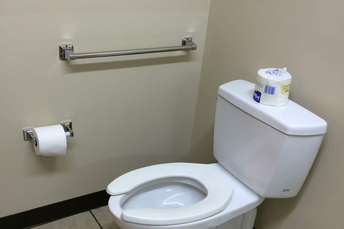 Des toilettes blanches, avec un porte-serviettes en papier et du papier toilette accroché au mur.