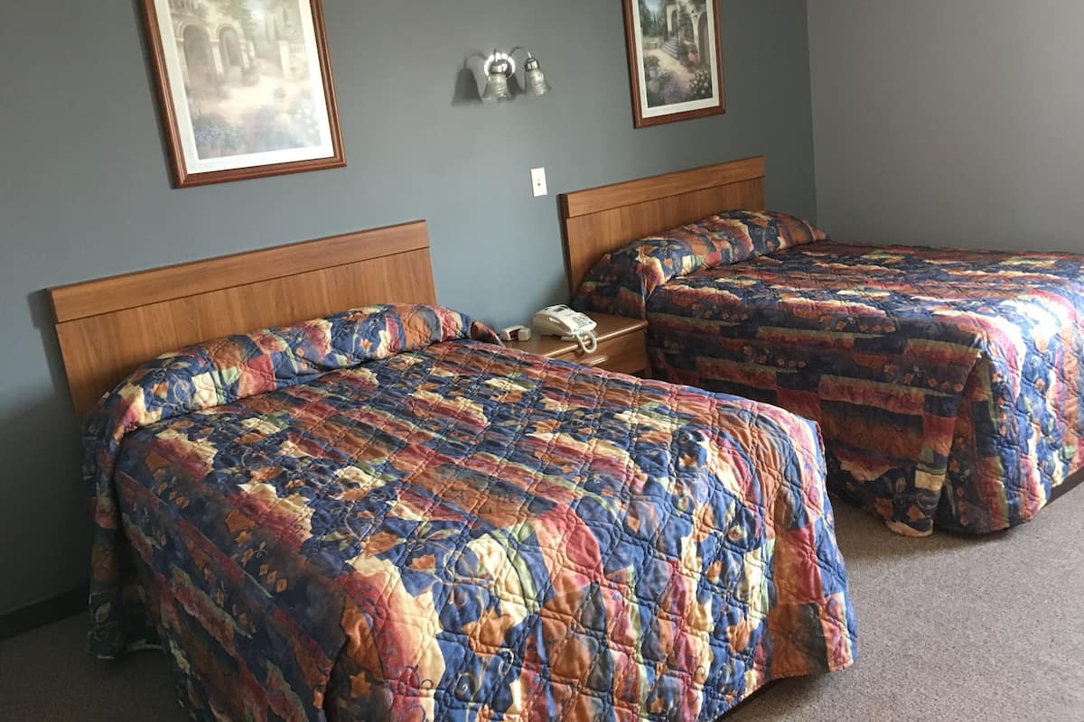 Une chambre avec deux lits, chacun recouvert d’une courtepointe à motifs floraux, dotée de têtes de lit en bois et d’une table de chevet avec un téléphone.