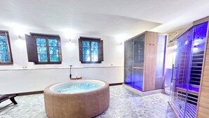 Ein Wellnessraum mit Whirlpool, Glasdusche und Holzzimmer für die Sauna.